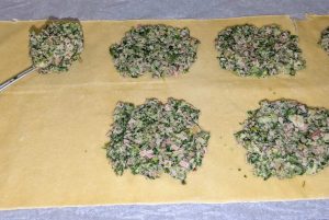 Mit einem Esslöffel wird die Füllung auf dem Nudelteig platziert.