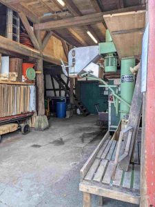 Blick in die Kelter. Rechts die Raspel und das Wasserbad, der Portionierer im Hintergrund die Presse. Links der Plattenwagen mit den Pressgittern.